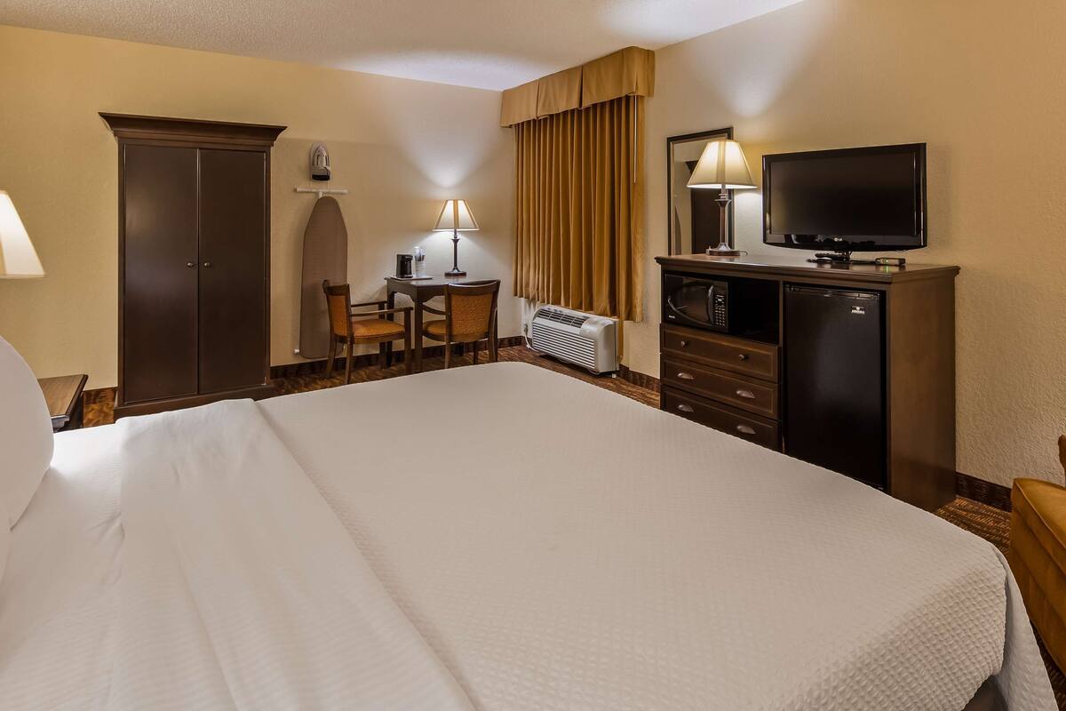 A hotel room with a large bed, a desk with a chair, a television, a minibar, and a wardrobe.