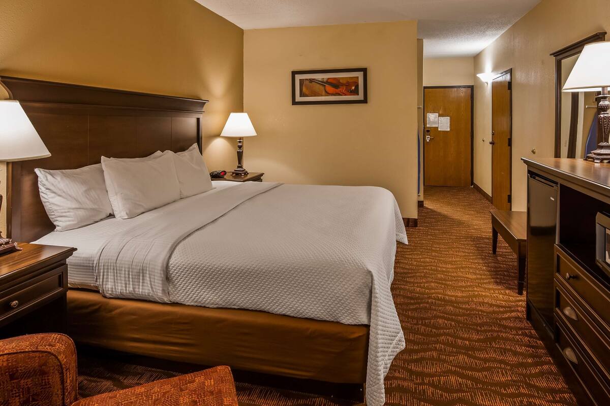 A hotel room with a large bed, a desk with a lamp, a dresser, and a television.