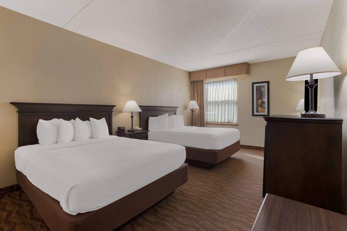 A hotel room with two beds, a desk, and a lamp.