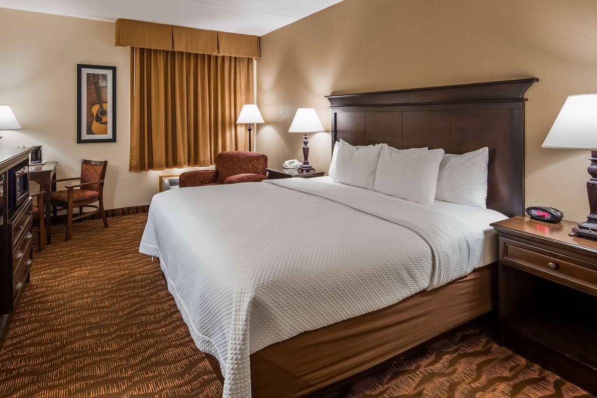 A hotel room with a large bed, two bedside tables with lamps, a desk with a chair, a small table with a phone, a chair, and a framed picture on the wall.