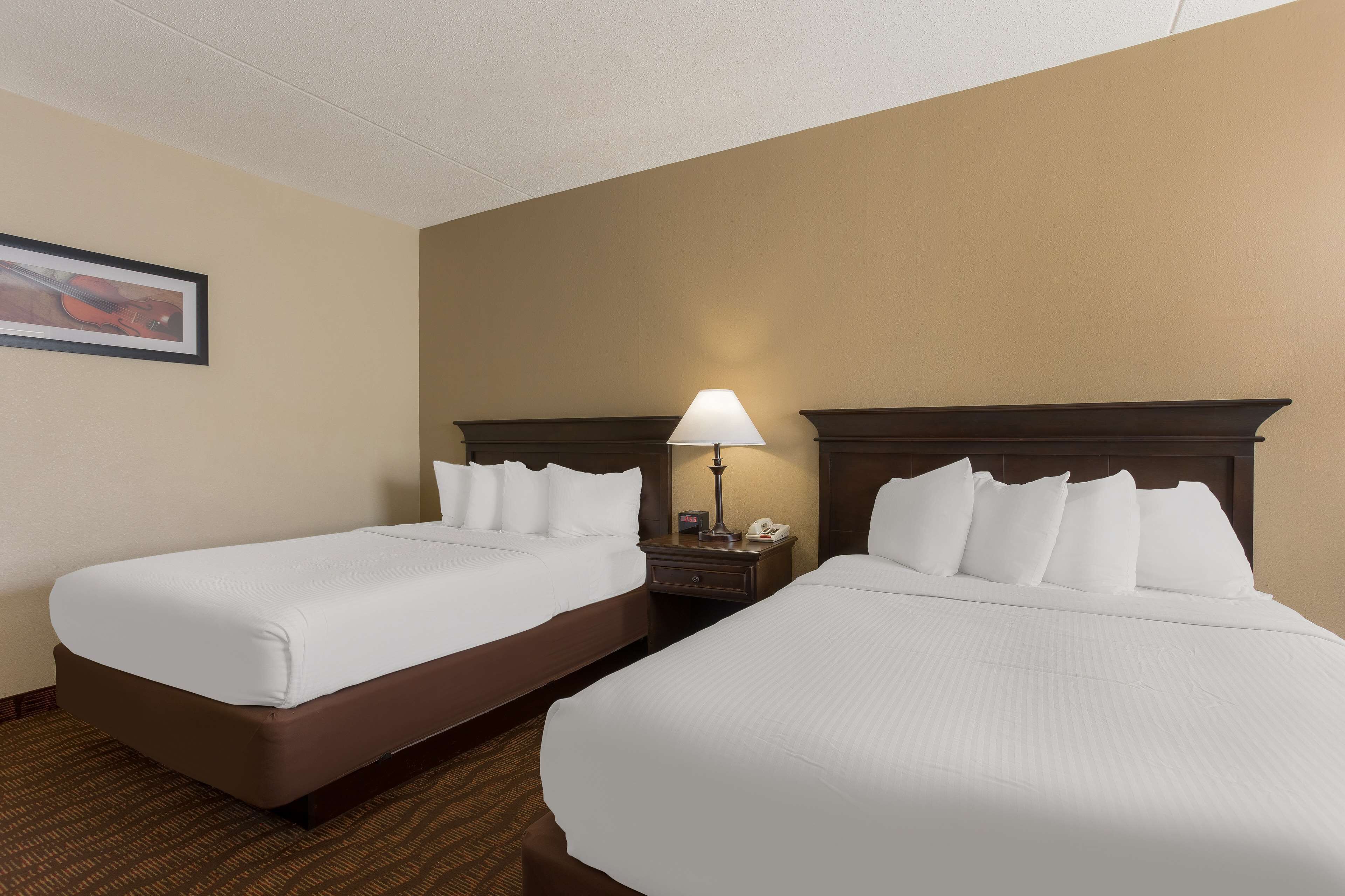 A hotel room with two single beds, a nightstand with a lamp, and a framed picture on the wall.