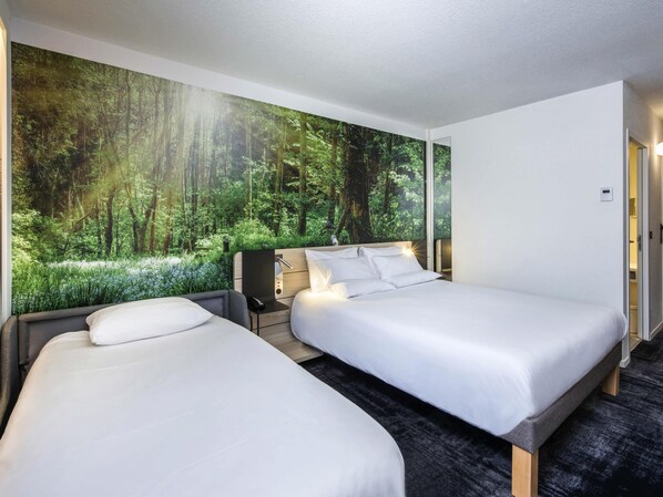 A hotel room with two beds, a desk, and a large forest mural on the wall.