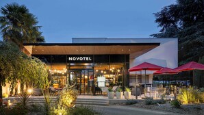 Un hotel moderno con fachada de vidrio, mobiliario exterior y una entrada bien iluminada.