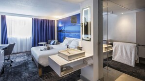 Una habitación de hotel moderna con una cama grande, un escritorio, un baño con ducha de vidrio y vista al mar.