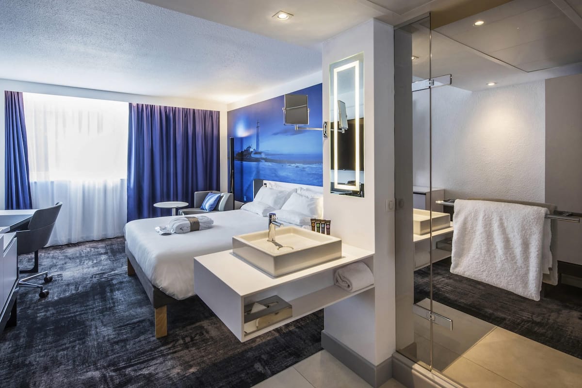 Ein modernes Hotelzimmer mit einem großen Bett, einem Schreibtisch, einem Badezimmer mit Glasdusche und Meerblick.