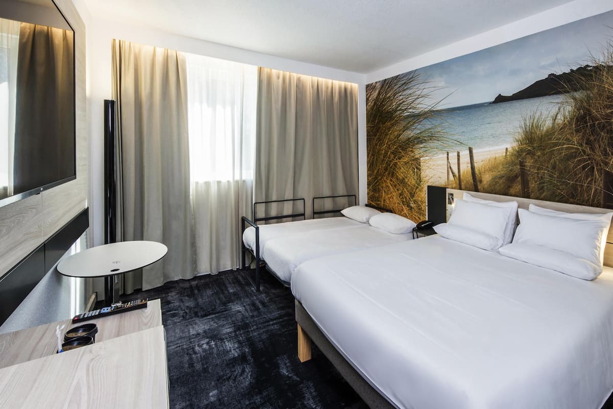 A hotel room with a bed, a TV, a desk, and a painting of a beach scene.