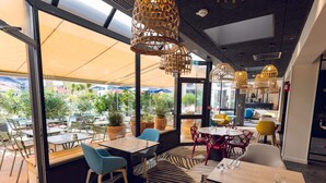 Un comedor interior con mesas y sillas, ventanas amplias y lámparas de mimbre colgantes.