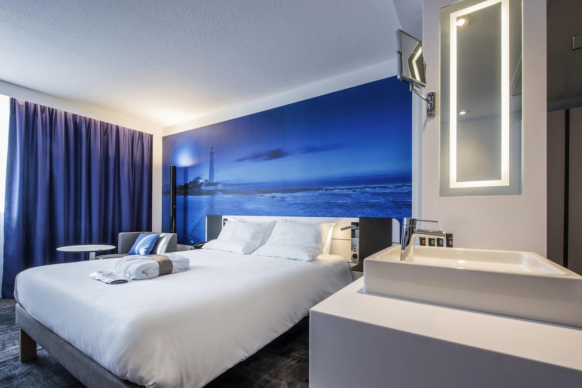 A hotel room with a large bed, a bedside table, a bathroom with a sink, and a wall mural of a lighthouse.