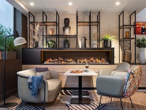 A modern living room with a fireplace, seating, and decorative shelves. - Novotel Rennes Alma (Rennes)