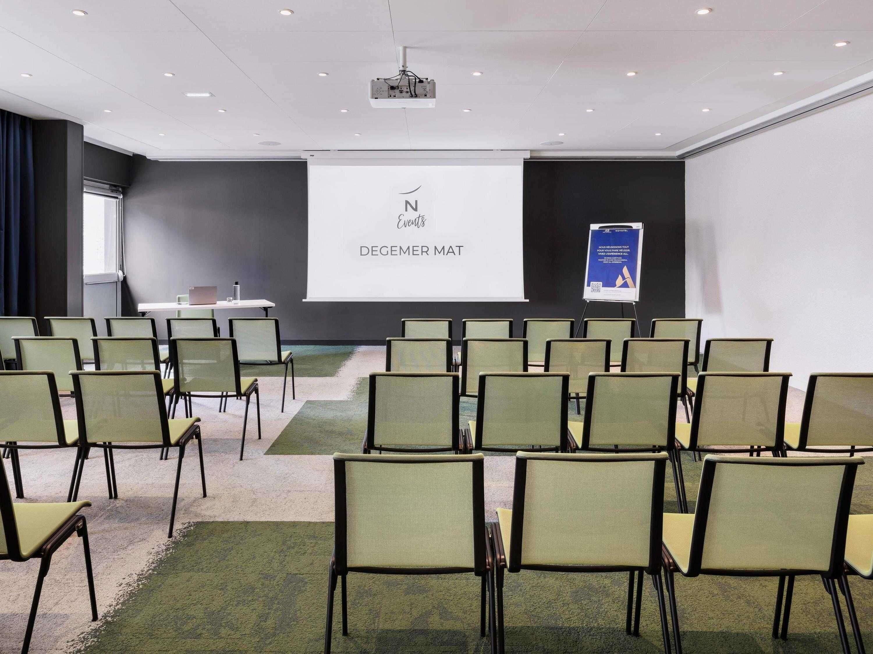 Een vergaderzaal met rijen stoelen, een scherm voor een beamer en een presentatiebord.