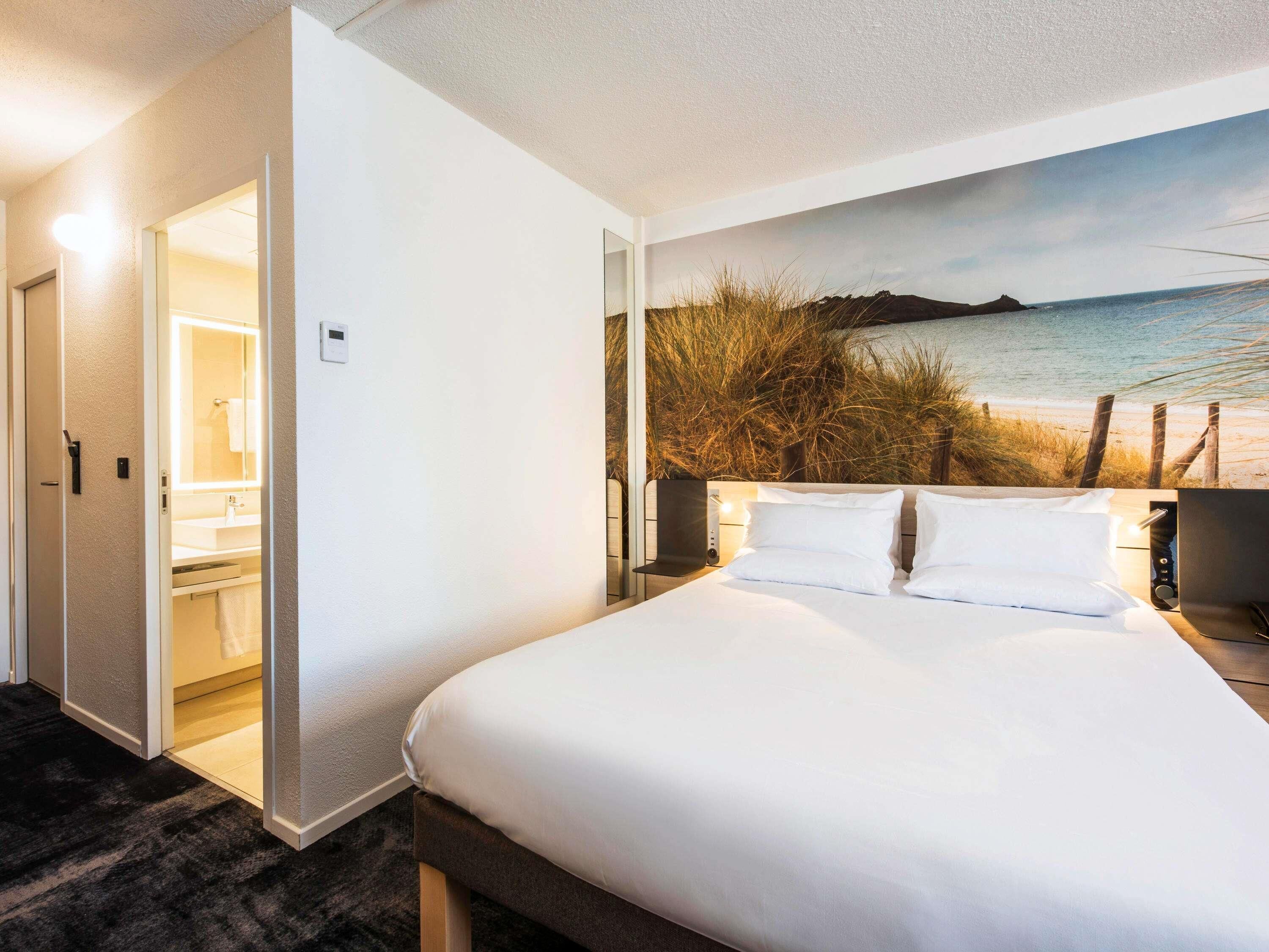 Et hotelværelse med seng, badeværelse og et muralmaleri med havudsigt.