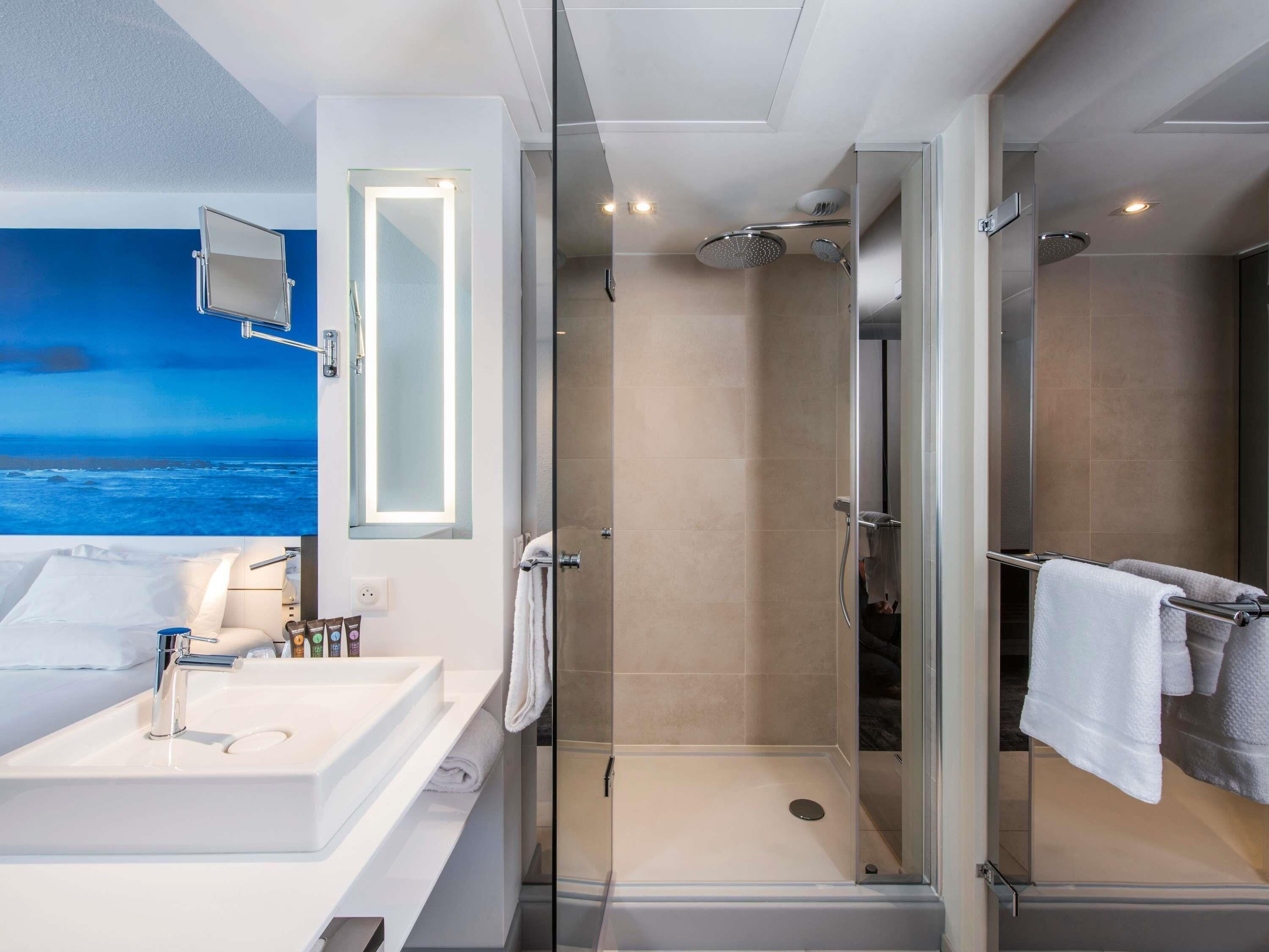 A modern bathroom with a glass-enclosed shower, a large mirror, and a view of the ocean.