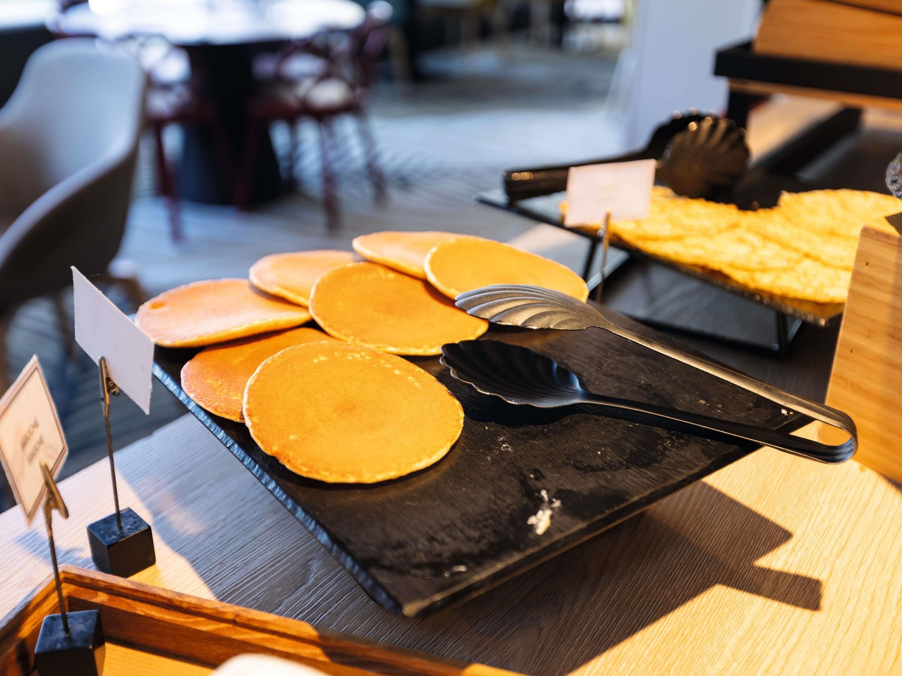 A breakfast buffet with pancakes and a pie, with a black serving tray and a spatula.