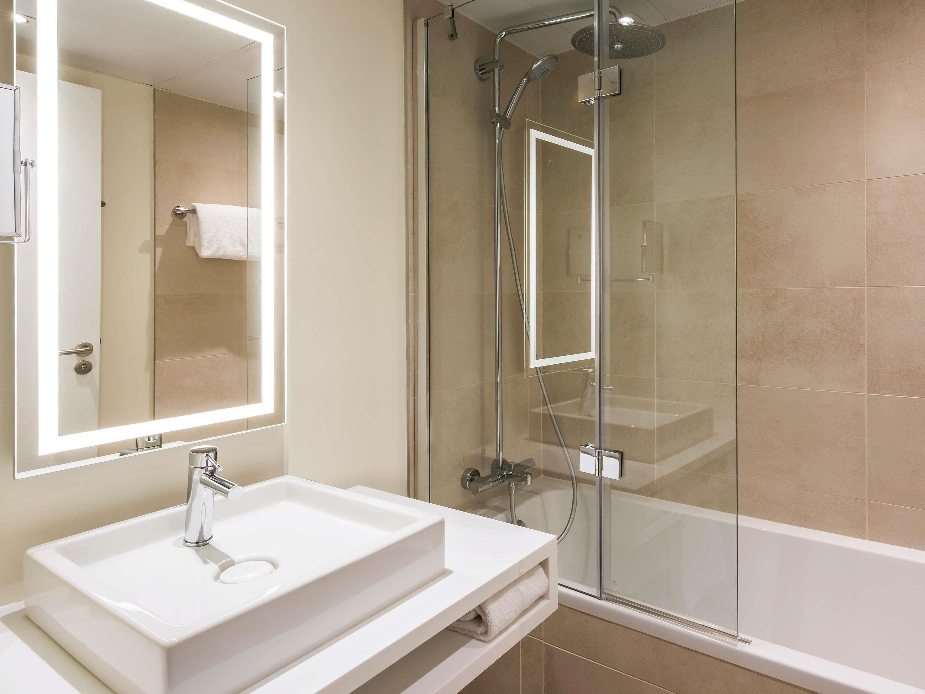 A modern bathroom with a glass-enclosed shower, a white sink, and a large mirror with integrated lighting.