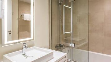 A modern bathroom with a glass-enclosed shower, a white sink, and a large mirror with integrated lighting.