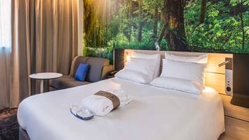 Een hotelkamer met een groot bed, een klein tafeltje, een stoel en een wanddecoratie met een bosmotief.