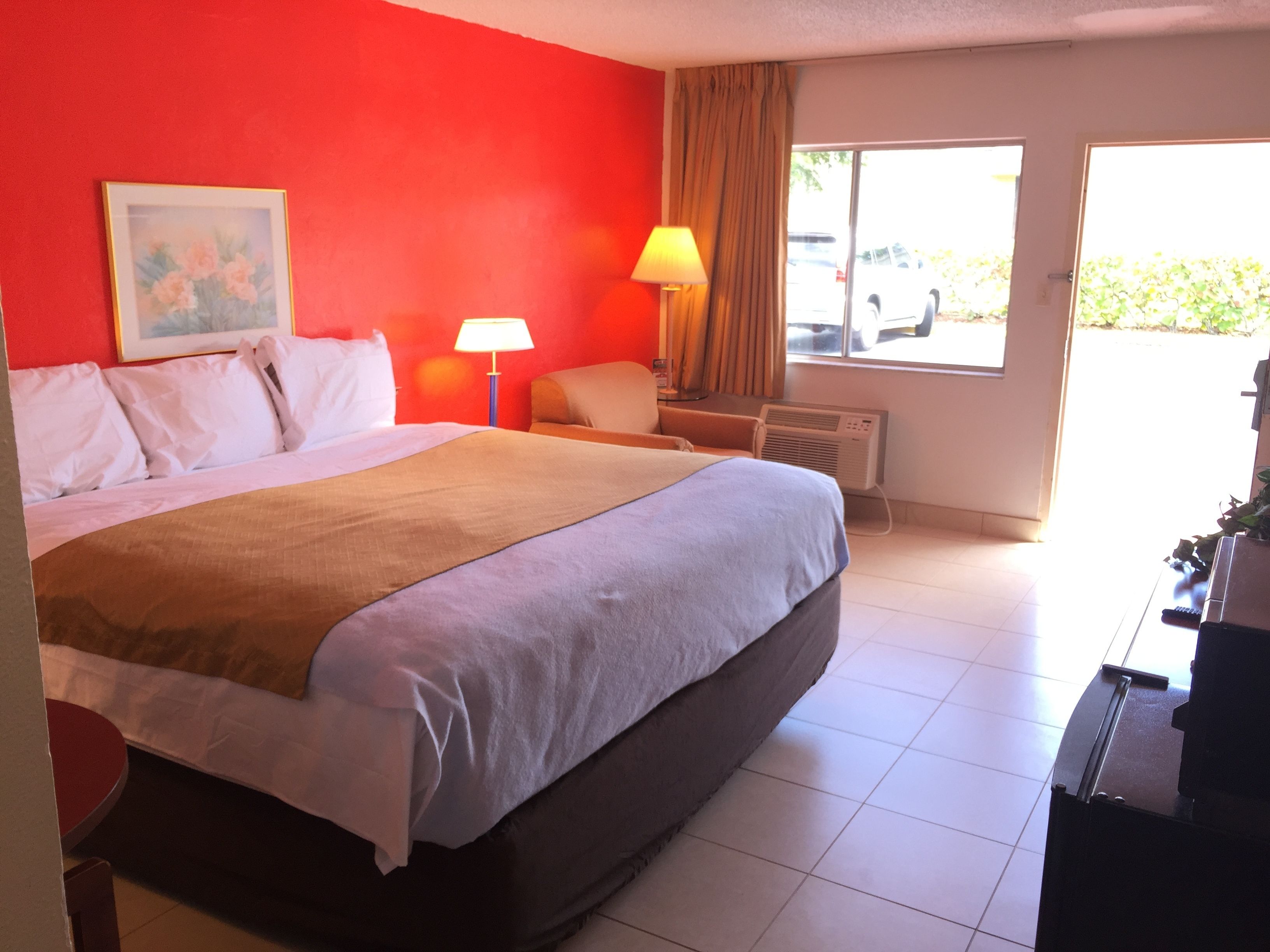 Habitación de hotel con una cama grande, un escritorio, una silla, una lámpara y una ventana con vistas al exterior.