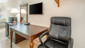 Una camera d'albergo con una scrivania in legno, una poltrona in pelle nera, un televisore a schermo piatto e una lampada.