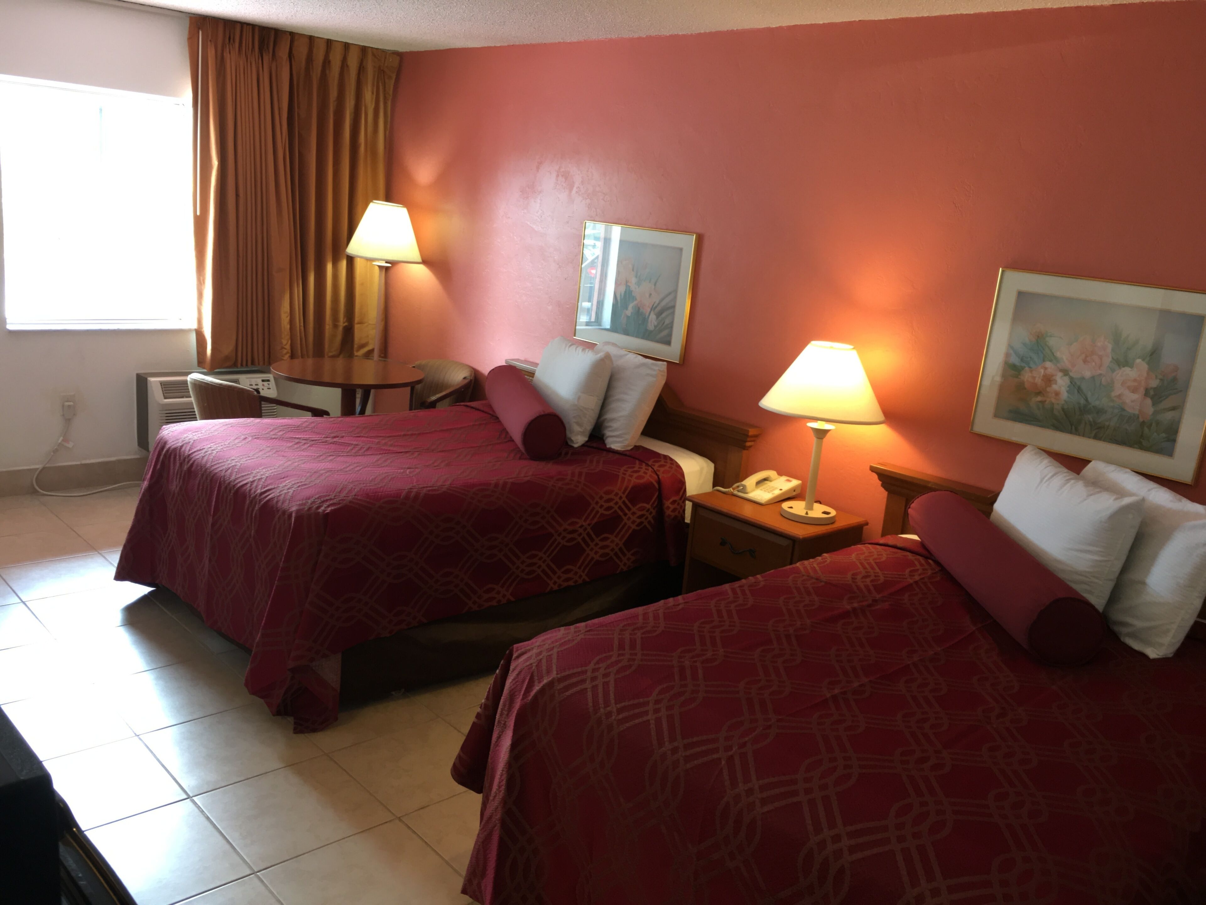A hotel room with two beds, a desk, a chair, a telephone, and a painting on the wall.