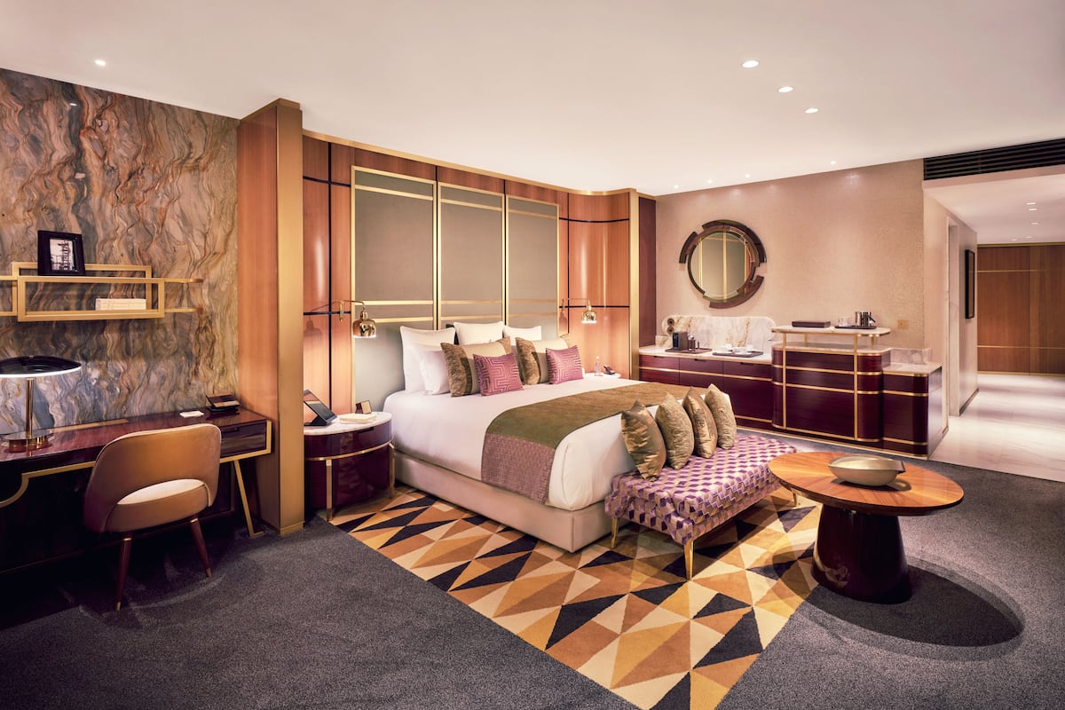 A modern hotel room with a large bed, a desk, a vanity, and a round mirror.