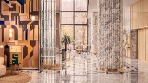 Un hall d’entrée spacieux au design moderne, avec une structure murale géométrique, une grande paroi en verre et un sol en marbre.