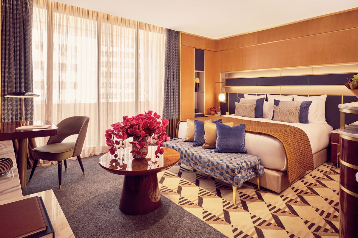 A hotel room with a bed, bedside table, chair, and a small table with a vase of flowers.