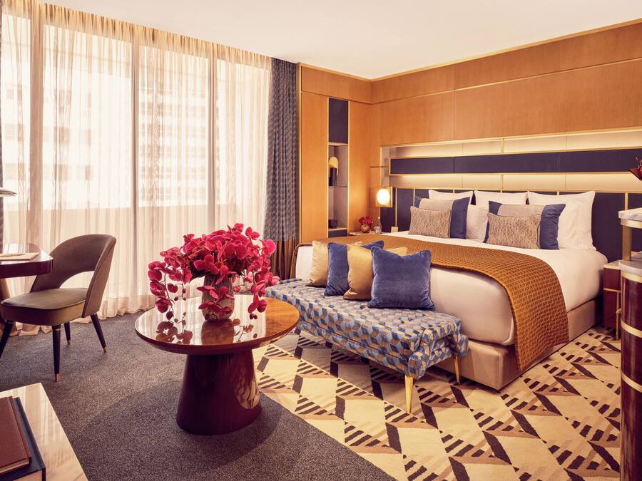 Habitación de hotel con cama, mesita de noche, silla y una pequeña mesa con un florero.