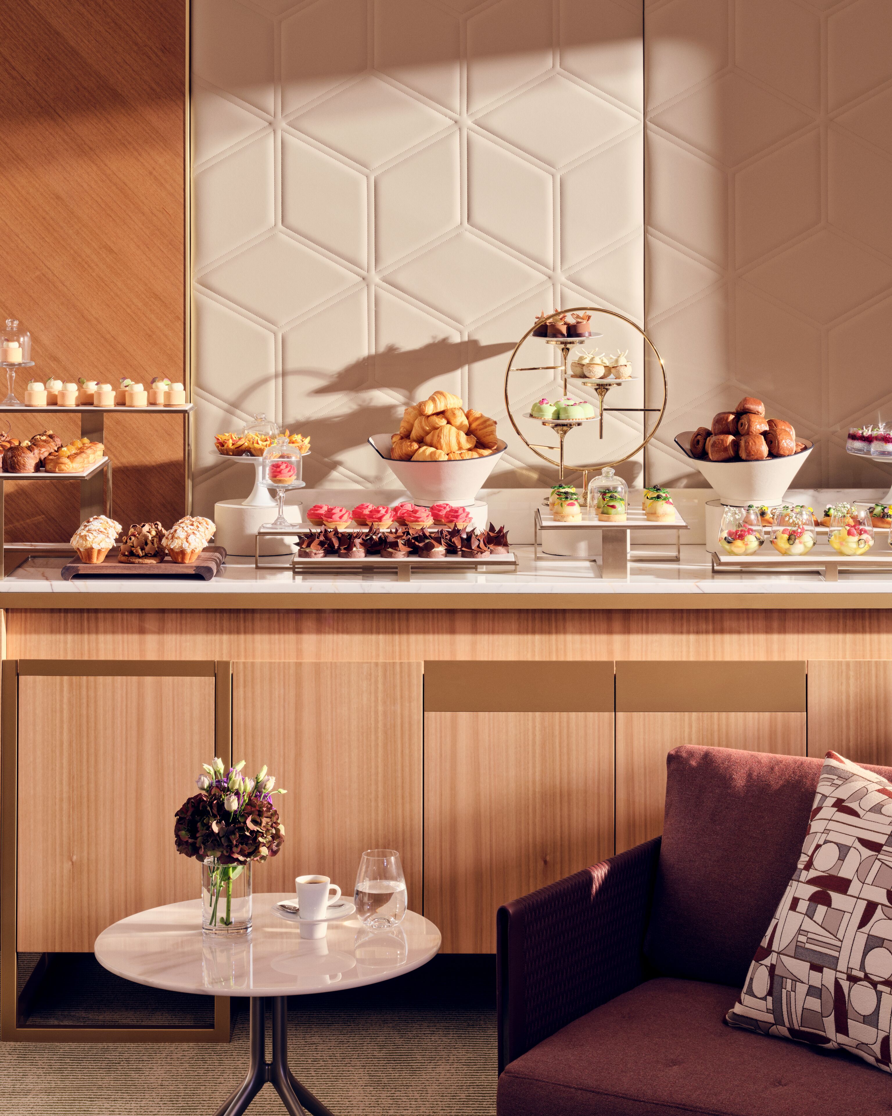 En frukostbuffé med ett urval av bakverk och desserter, ett runt bord med en vas med blommor och en bekväm sittgrupp med mjuka kuddar.