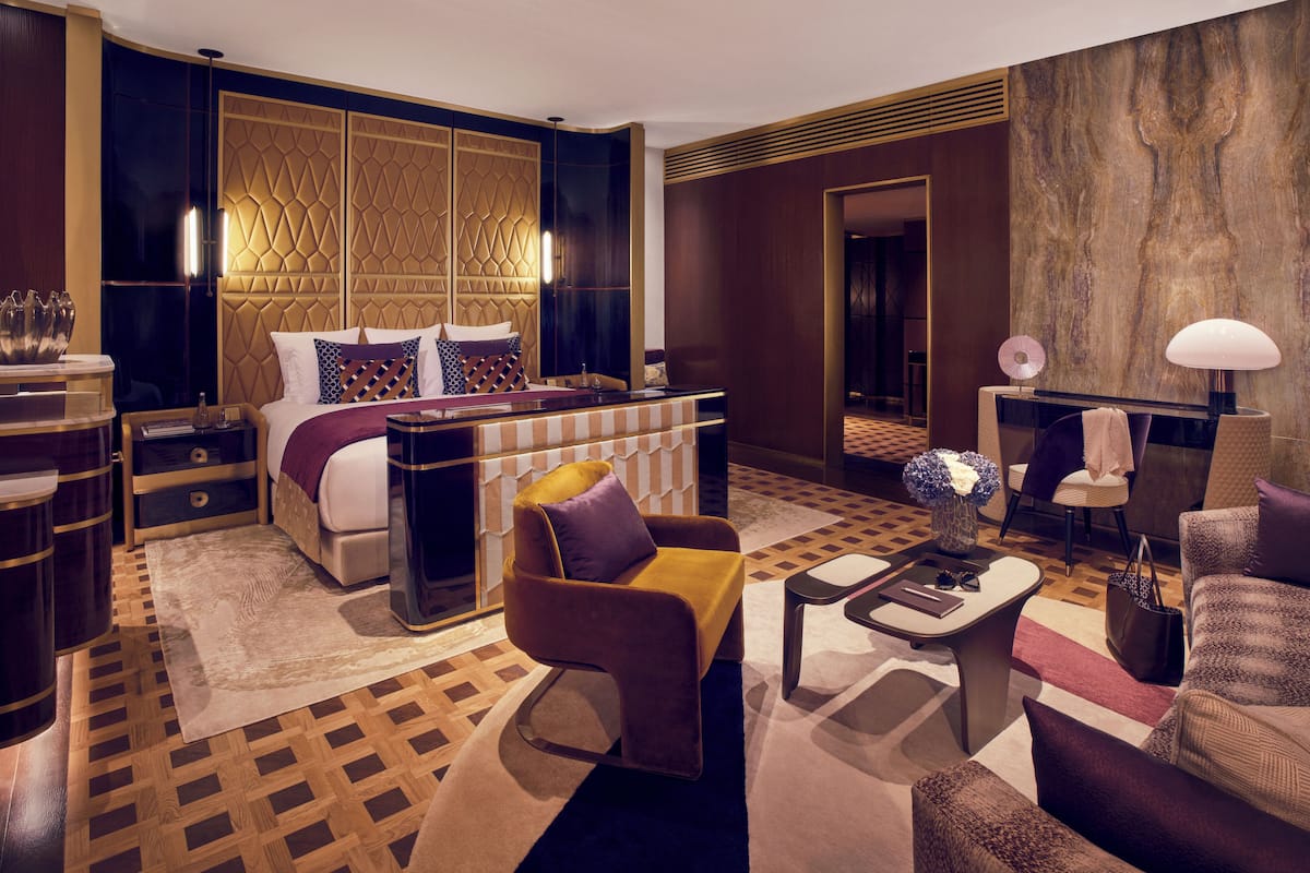 A modern hotel room with a large bed, a sofa, a coffee table, and a desk with a lamp.
