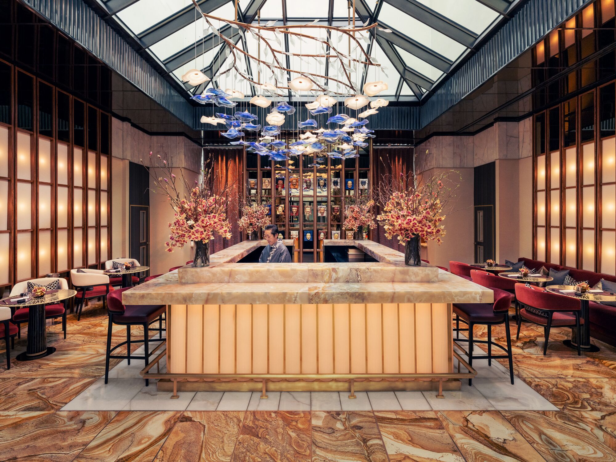 A spacious lobby with a central reception desk, marble flooring, and a high ceiling with a skylight.