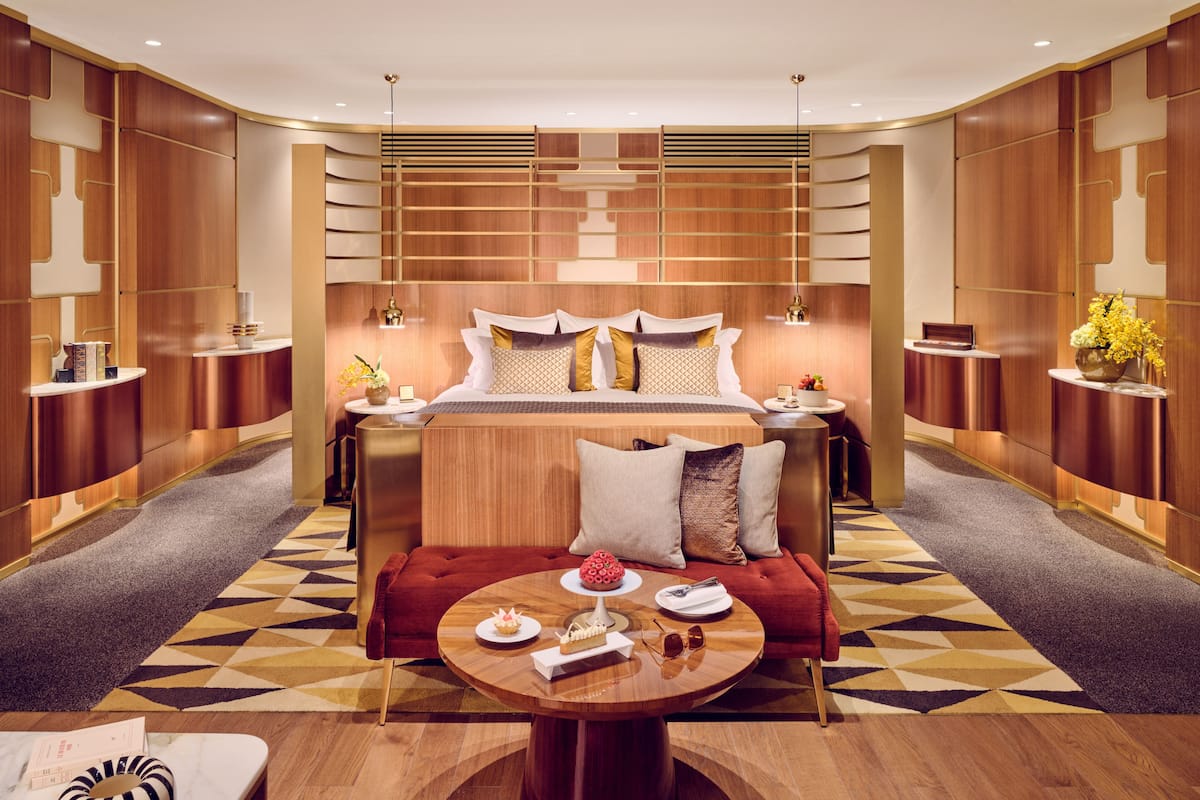 A modern hotel room with a large bed, a red sofa, a round coffee table, and a geometric patterned carpet.