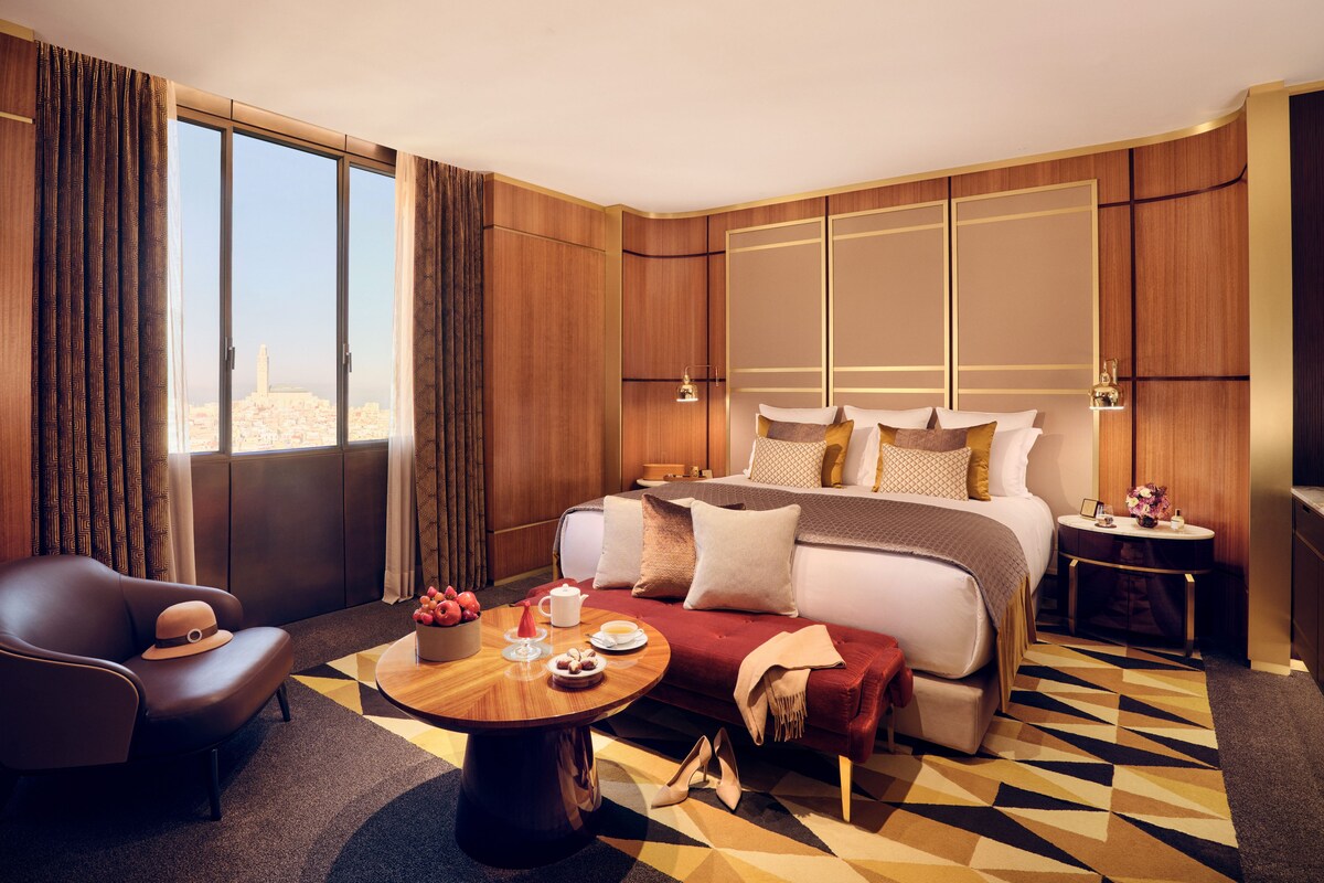 Habitación de hotel con una cama grande, un sofá, una mesa de centro redonda y vistas a la ciudad.