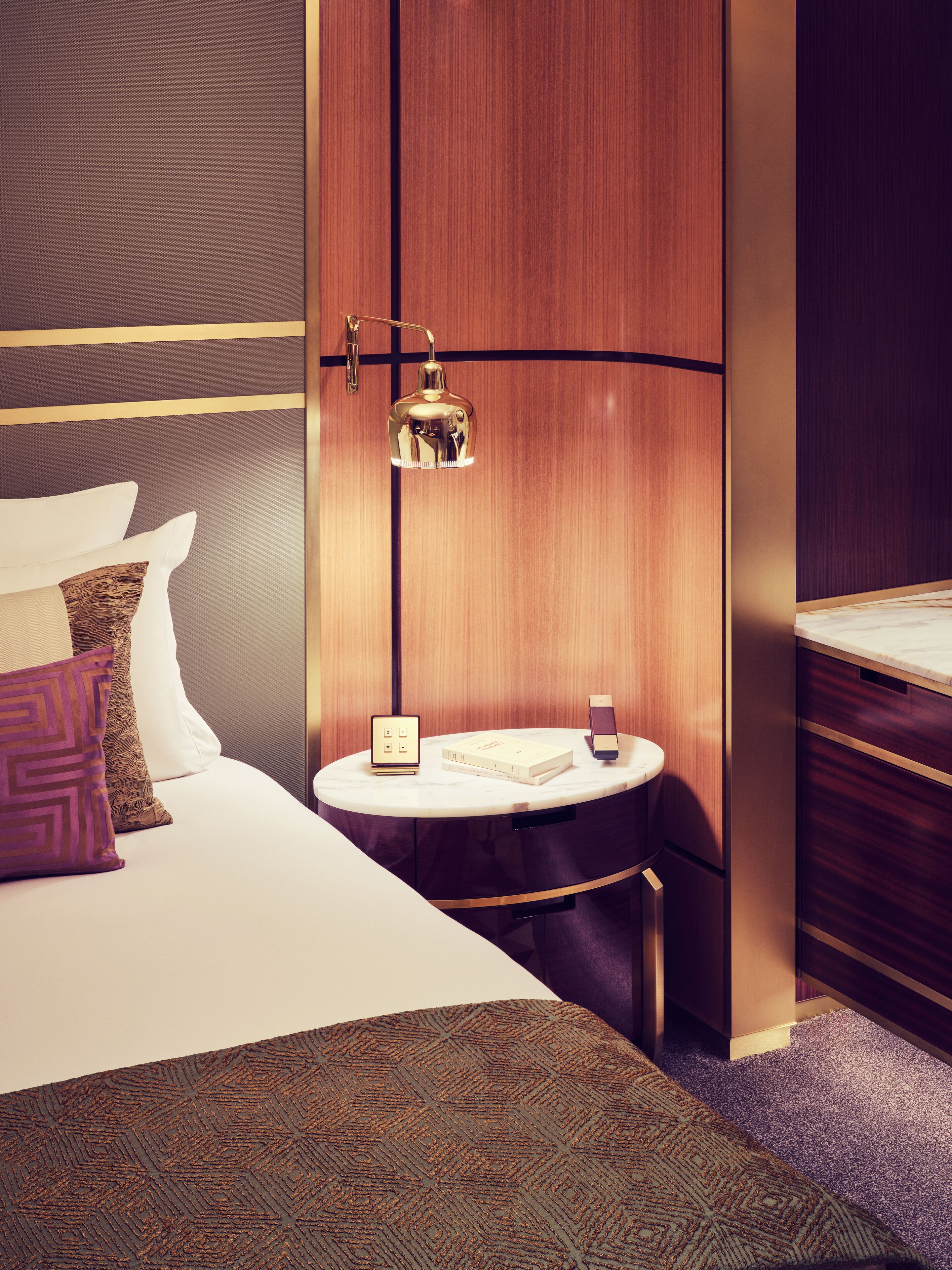 A hotel room with a bed, bedside table, lamp, and a small round table with a book and a phone.