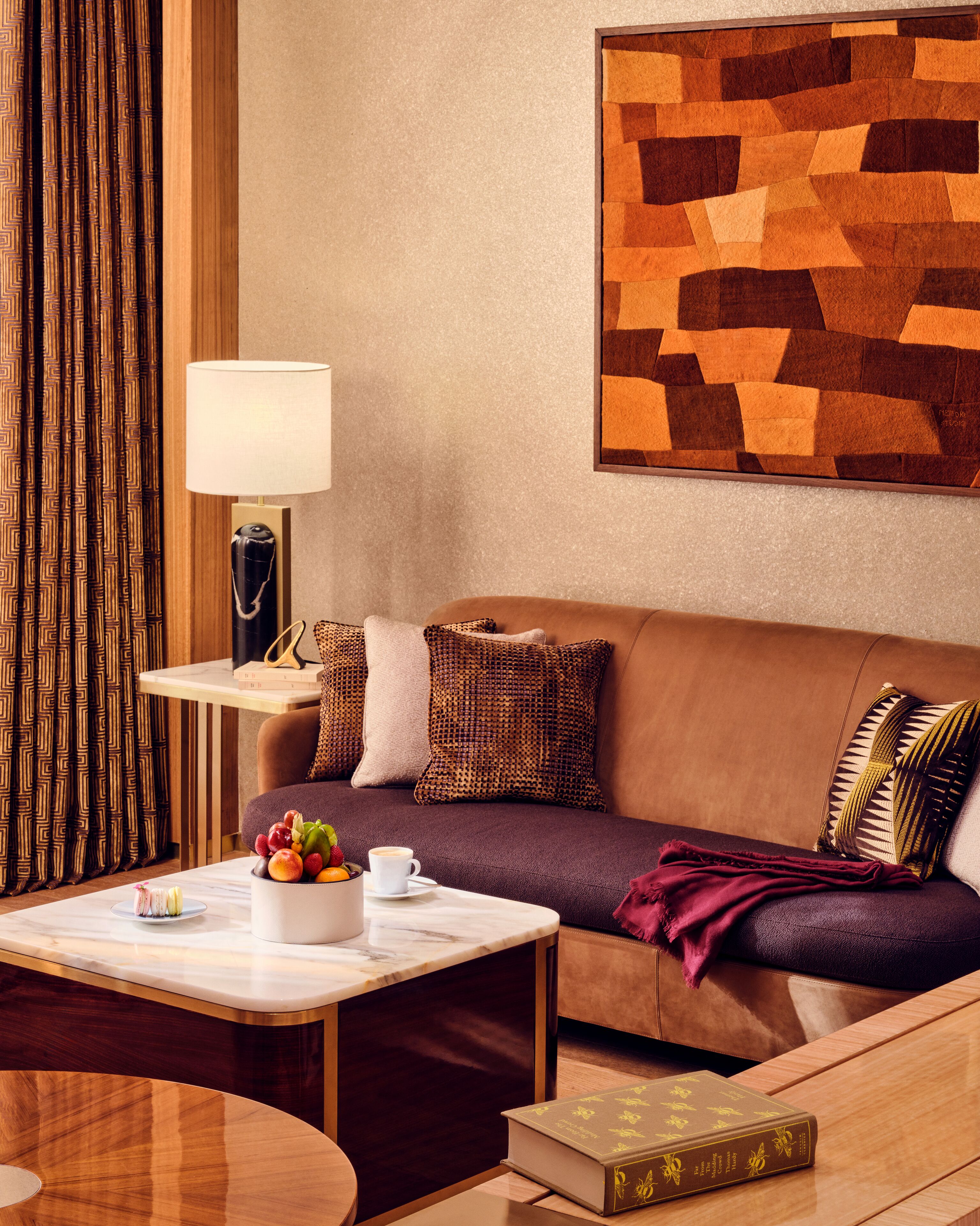 A modern living room with a sofa, a coffee table with fruits and a cup, a lamp, and a wall art piece.
