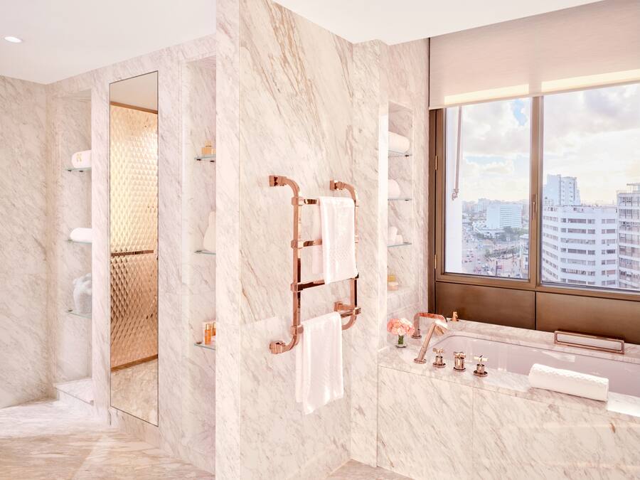 Un baño moderno con paredes de mármol, un ventanal con vistas a la ciudad, una bañera y un tocador con espejo.