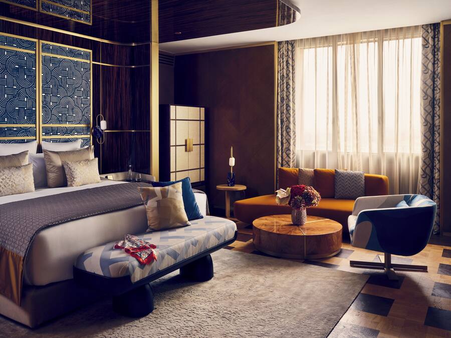 Moderni hotellihuone, jossa on suuri sänky, sohva, sohvapöytä ja tuoli. Huoneessa on ikkuna, jossa on verhot, ja ikkunasta on näkymä ulos.
