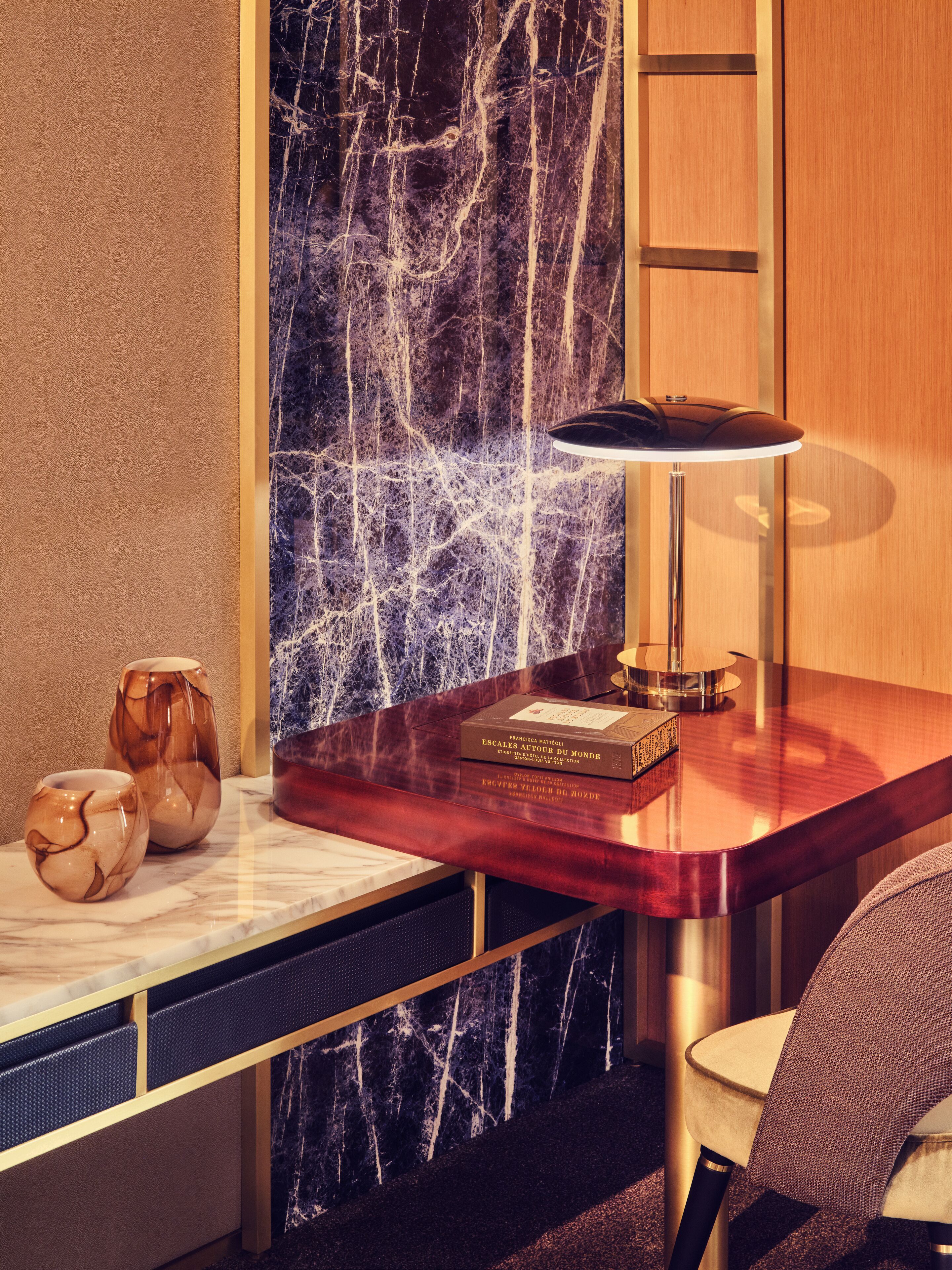 Een moderne kamer met een marmeren wand, een houten bureau, een stoel en een bureaulamp.