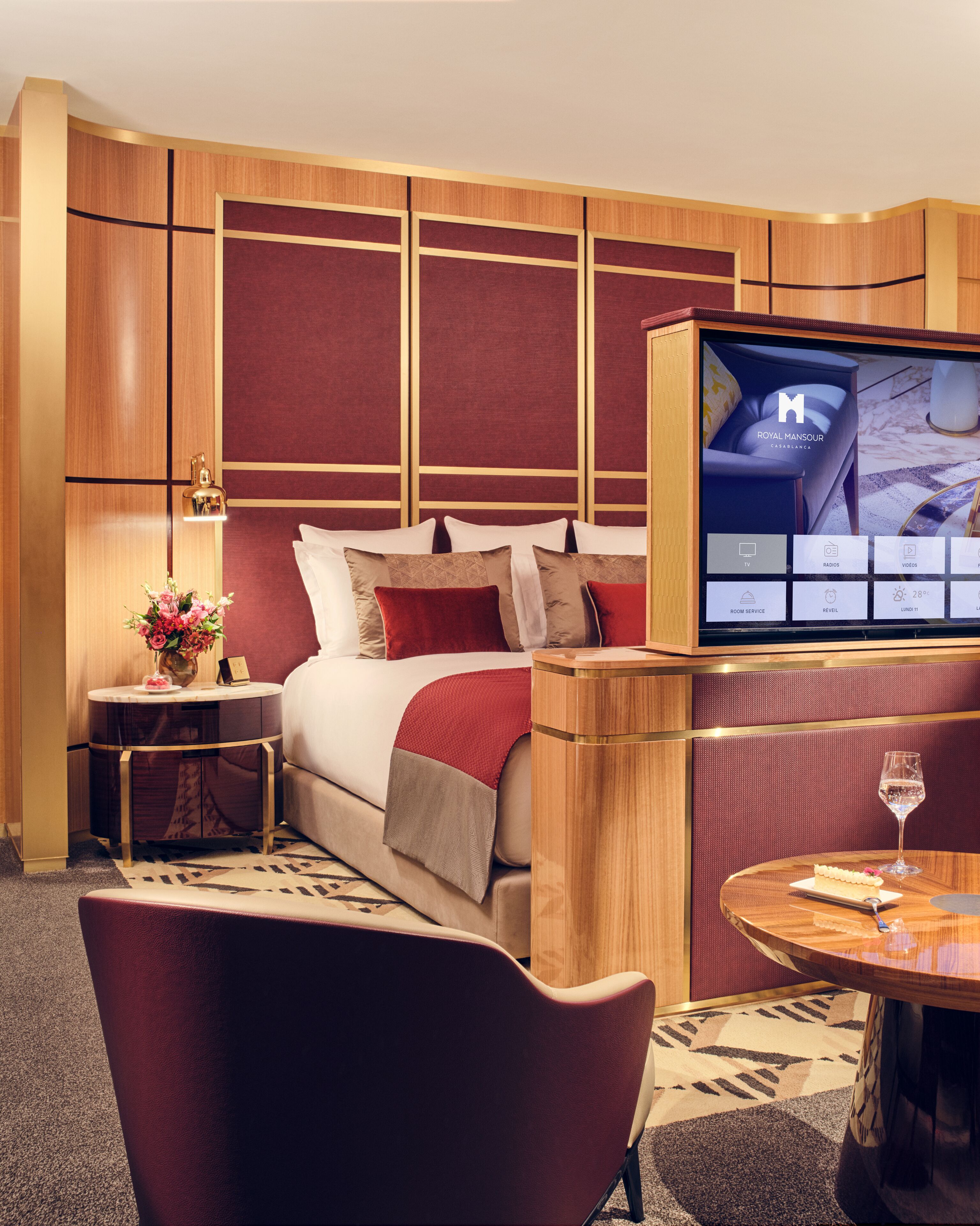 A hotel room with a bed, a TV, a small table with a glass of wine, and a chair.