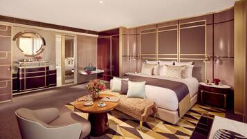 A modern hotel room with a large bed, a sitting area with a table, a vanity with a mirror, and a walk-in closet.