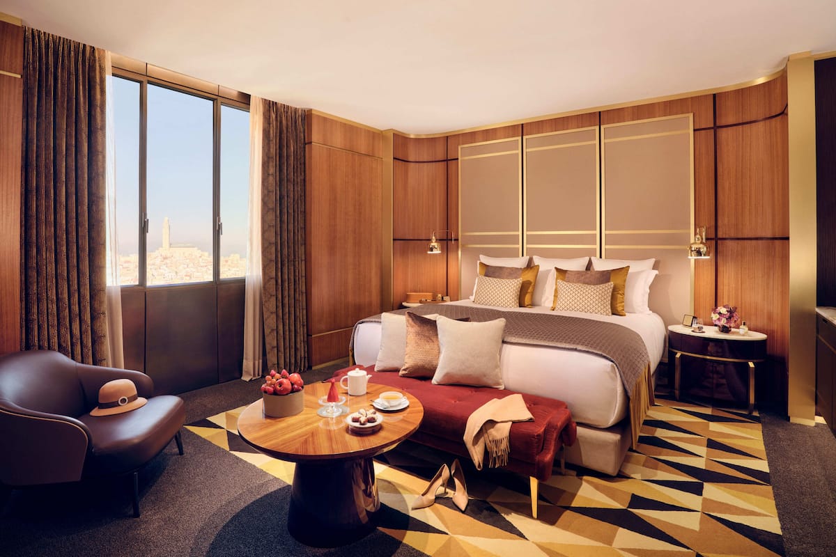 A hotel room with a large bed, a sofa, a round coffee table, and a view of the city.