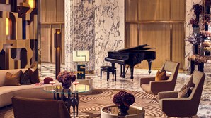 Un hall d’entrée luxueux avec un grand piano, des fauteuils confortables, une table basse en verre et un sol en marbre.