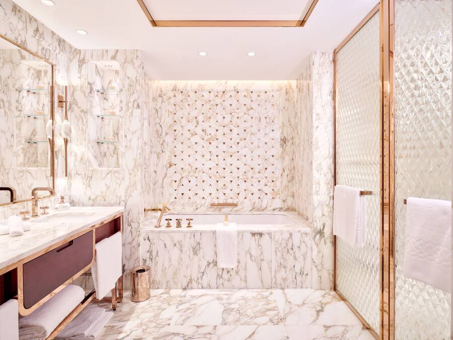 Un baño moderno con paredes de mármol, un espejo grande, una bañera y una zona de ducha.