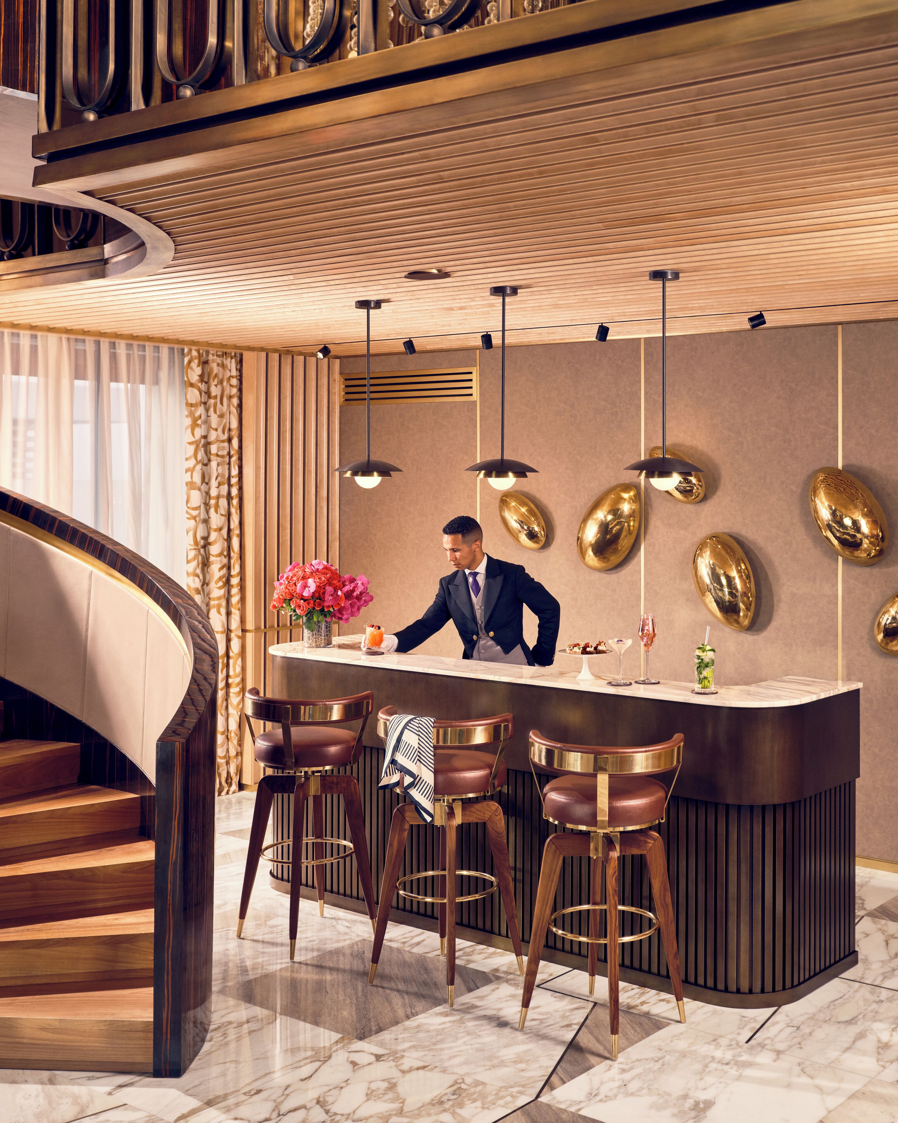 Un espace bar moderne avec un barman, un sol en marbre et un escalier doté de rampes en bois.