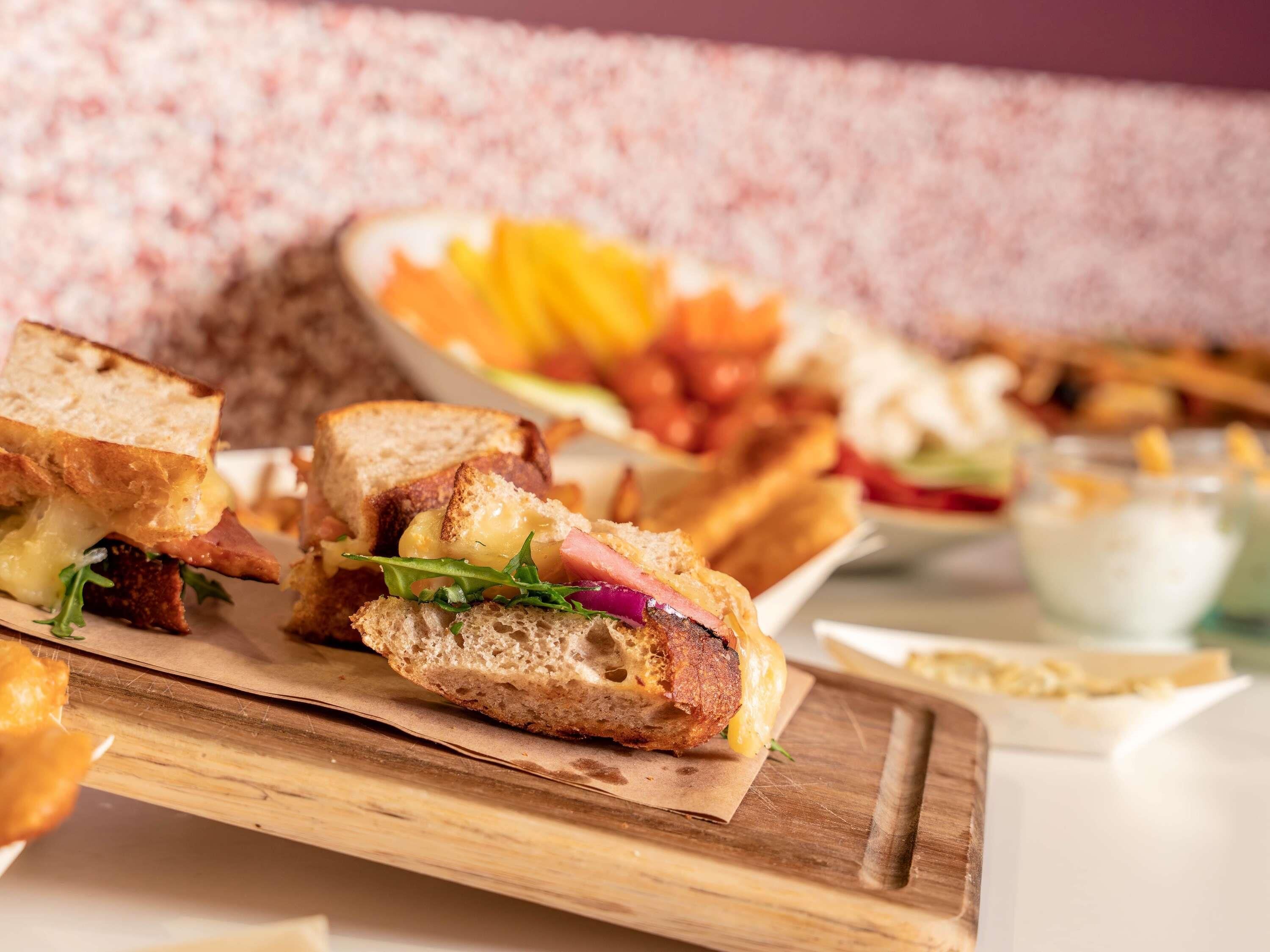 Un sandwich dont on voit bien la garniture, une assiette de frites et un bol de sauce, le tout présenté sur une planche en bois.