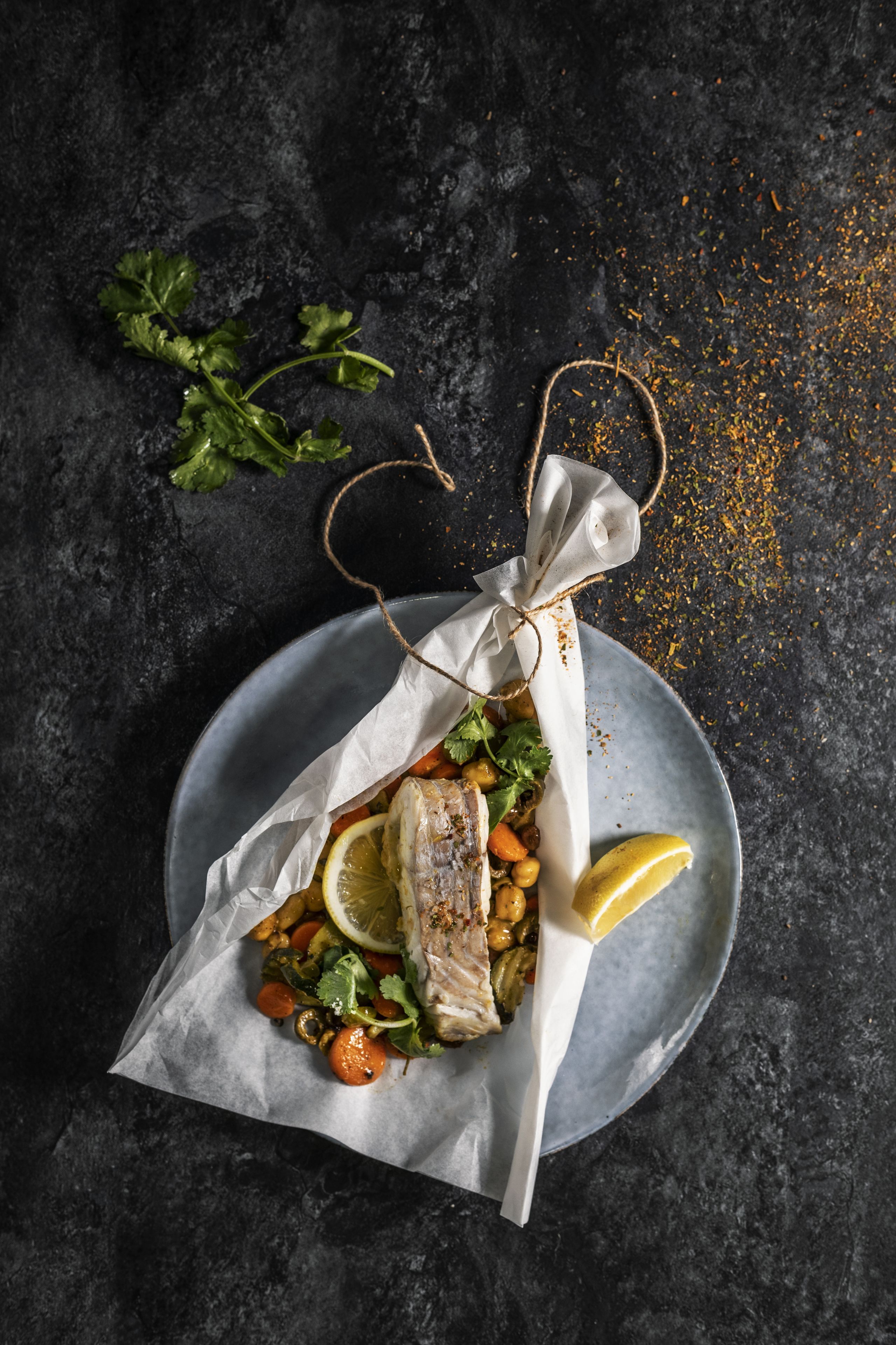 Une assiette de poulet rôti, accompagné de légumes et de citron, posée sur une surface sombre.