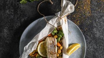 Une assiette de poulet rôti, accompagné de légumes et de citron, posée sur une surface sombre.