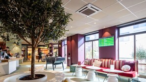 A modern hotel lobby with a reception desk, seating area, and a large window. - Hotel ibis Lille Centre Gares (Lille)