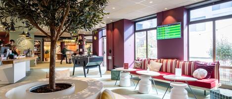 A modern hotel lobby with a reception desk, seating area, and a large window.