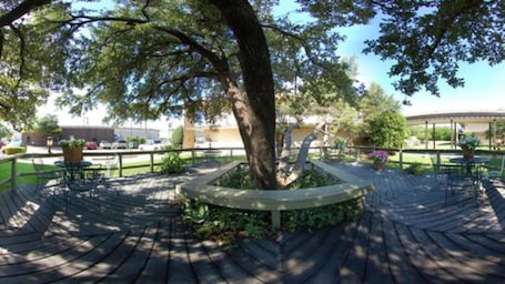 A wooden deck with a circular seating area, surrounded by trees and a building in the background.