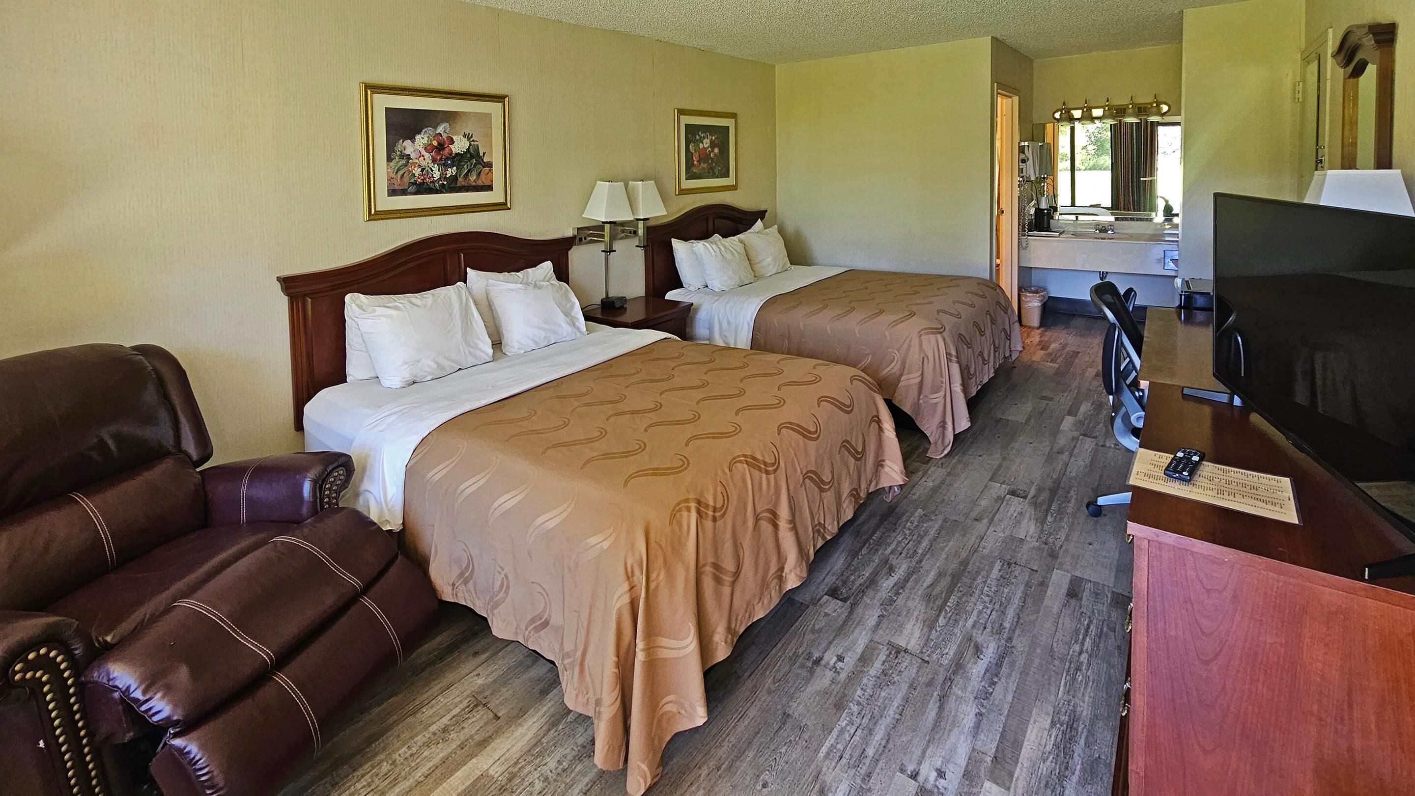 A hotel room with two beds, a TV, a desk with a computer, and a chair.